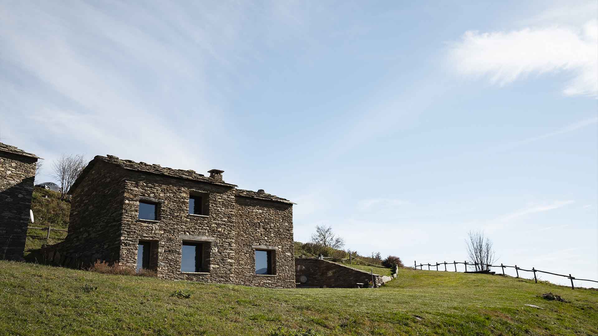 Edificio in pietra ristrutturato con finestre moderne e prato verde a Ostana