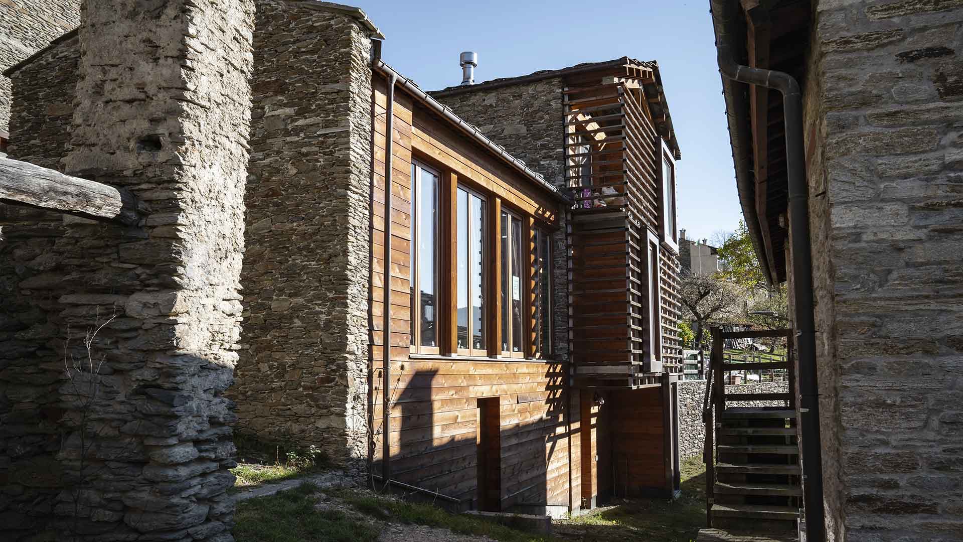 Edificio contemporaneo in legno e vetro tra le antiche costruzioni in pietra di Ostana