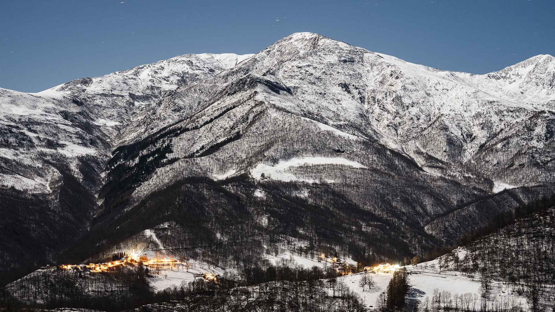 Veduta notturna di Ostana illuminata ai piedi delle montagne innevate