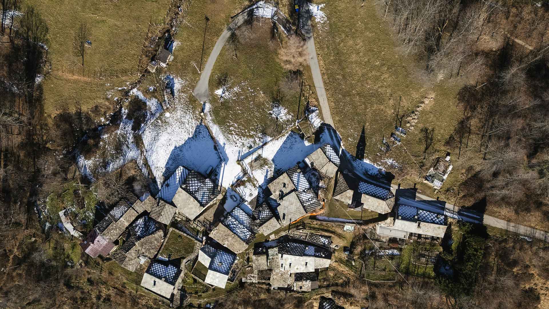 Vista aerea di una borgata di Ostana con tetti in lose scure, circondata dal bosco