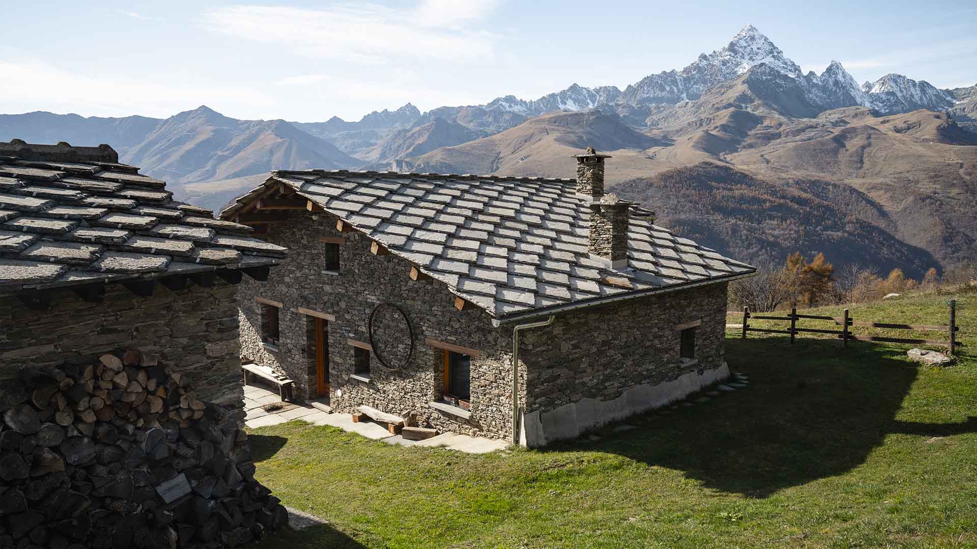 Casa rurale in pietra ristrutturata con tetto in lose e catasta di legna, vista sul Monviso e sulle cime alpine