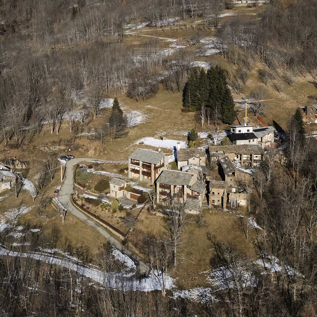 Vista aerea di una borgata a Ostana con la strada di accesso e il bosco circostante